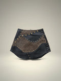 Falda corta Pampa Boho de piel negra y marrón con estoperoles y detalle de textura.